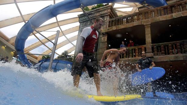 Drei Männer surfen auf künstlichen Wellen in einem Hallenbad.