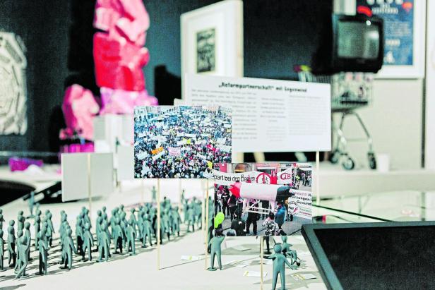 Eine Installation mit Miniaturfiguren und Fotos von Demonstrationen.