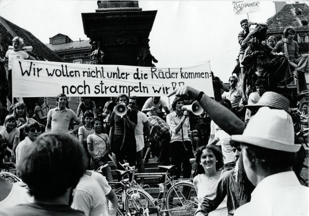 Eine Demonstration mit Fahrrädern und einem Transparent: „Wir wollen nicht unter die Räder kommen: noch strampeln wir!“.