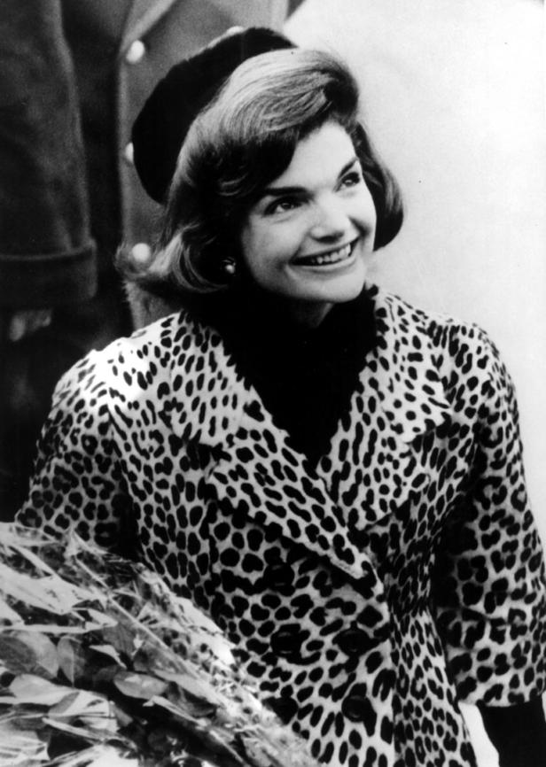 Jacqueline Kennedy in einem Leopardenmantel lächelt.