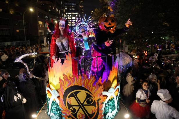 Drei Personen in Halloween-Kostümen stehen auf einem Wagen während einer Parade.