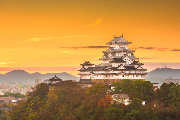 Der Himeji-jo, eine japanische Burg, thront auf einem Hügel unter einem orangefarbenen Himmel.