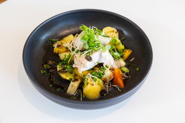 Ein Teller mit Fisch, Kartoffeln, Gemüse und Kräutern garniert.