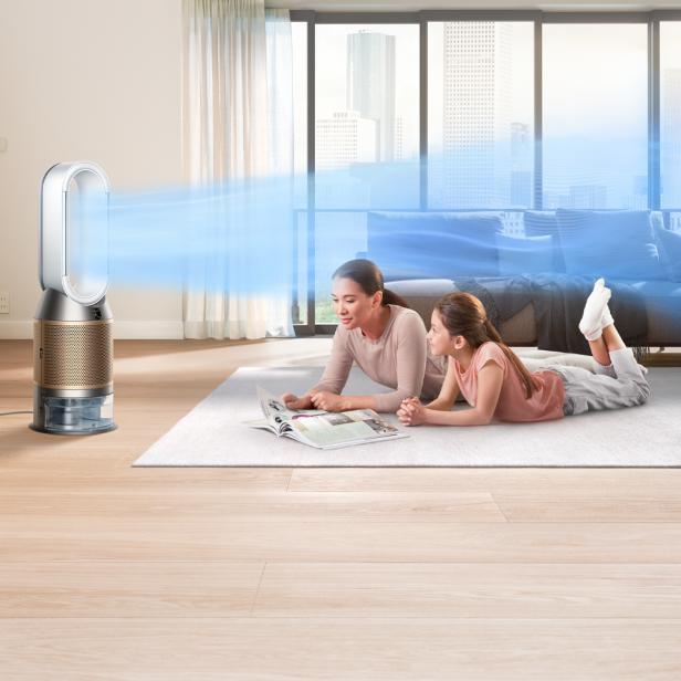 Eine Mutter und ihre Tochter liegen auf einem Teppich und lesen eine Zeitschrift, während ein Dyson-Luftreiniger läuft.