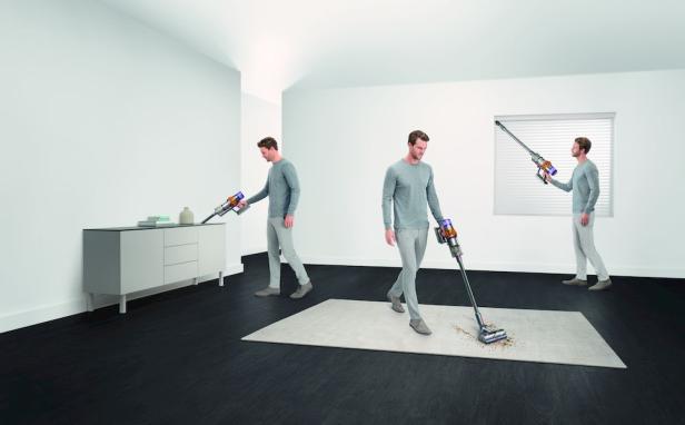 Ein Mann benutzt einen Dyson Staubsauger, um verschiedene Oberflächen in einem modernen Raum zu reinigen.