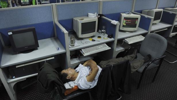 Ein Mann schläft in einem Büroraum zwischen Computern und Schreibtischen.