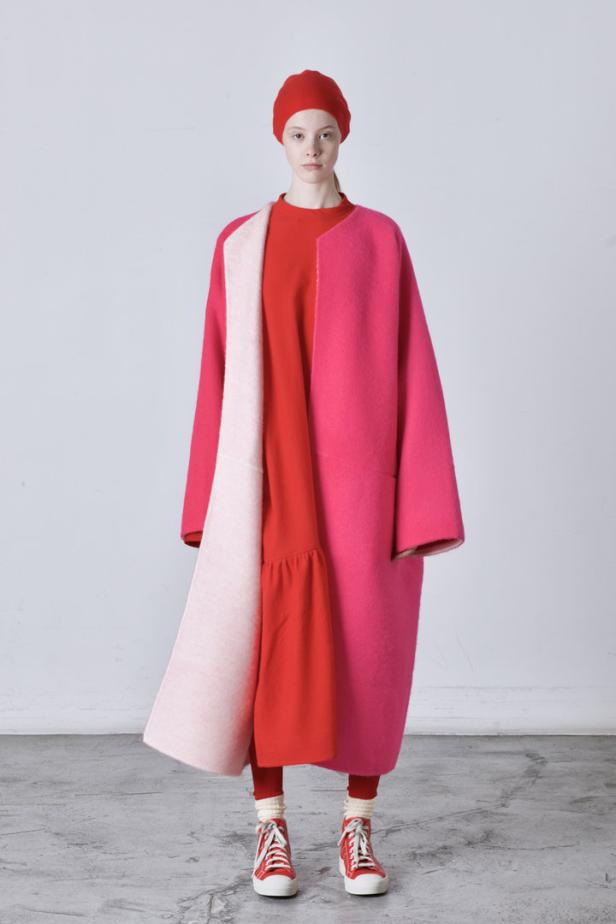 Ein Model trägt einen pinkfarbenen Mantel, ein rotes Kleid und rote Turnschuhe.