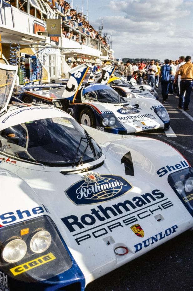 Mehrere Rothmans Porsche Rennwagen stehen in der Boxengasse.