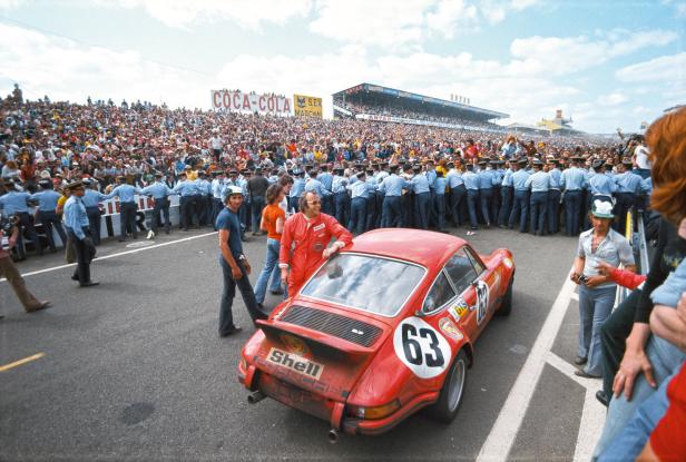 Ein roter Porsche 911 mit der Nummer 63 steht vor einer Menschenmenge bei einem Autorennen.