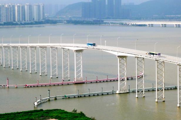 Zwei Busse fahren über eine lange, weiße Brücke über dem Wasser.
