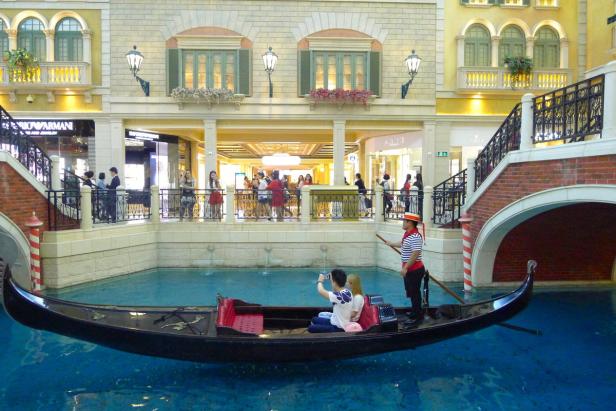 Eine Gondel fährt mit Touristen durch einen künstlichen Kanal in einem Einkaufszentrum.