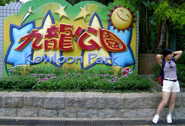 Eine Frau steht vor dem bunten Schild des Kowloon Parks in Hongkong.