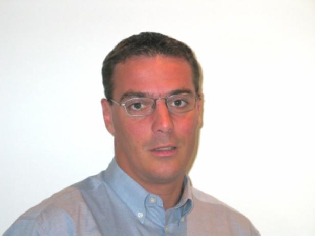 Ein Mann mit Brille und hellblauem Hemd vor einem weißen Hintergrund.