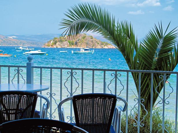 Blick von einer Terrasse auf das Meer mit Booten und einer kleinen Insel.