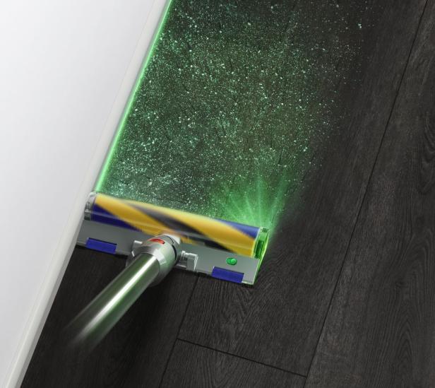 Ein Staubsauger mit Licht beleuchtet Staub auf einem dunklen Holzboden.
