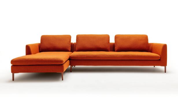 Ein orangefarbenes Ecksofa mit drei Kissen vor einem weißen Hintergrund.