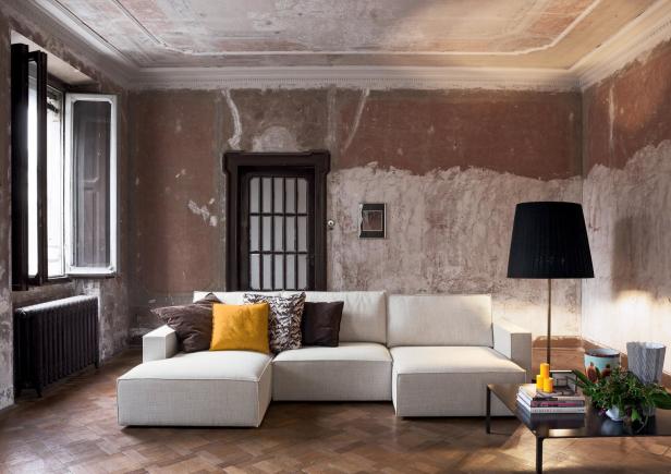 Ein helles Sofa mit Kissen steht in einem Zimmer mit Stuckdecke und Holzboden.