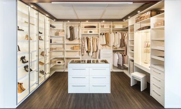 Ein begehbarer Kleiderschrank mit beleuchteten Regalen, Kleidung und Schuhen.