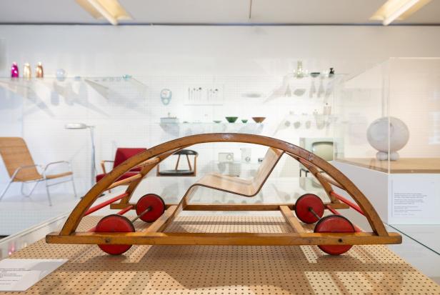 Ein hölzernes Spielzeugauto mit roten Rädern steht in einem Museum.