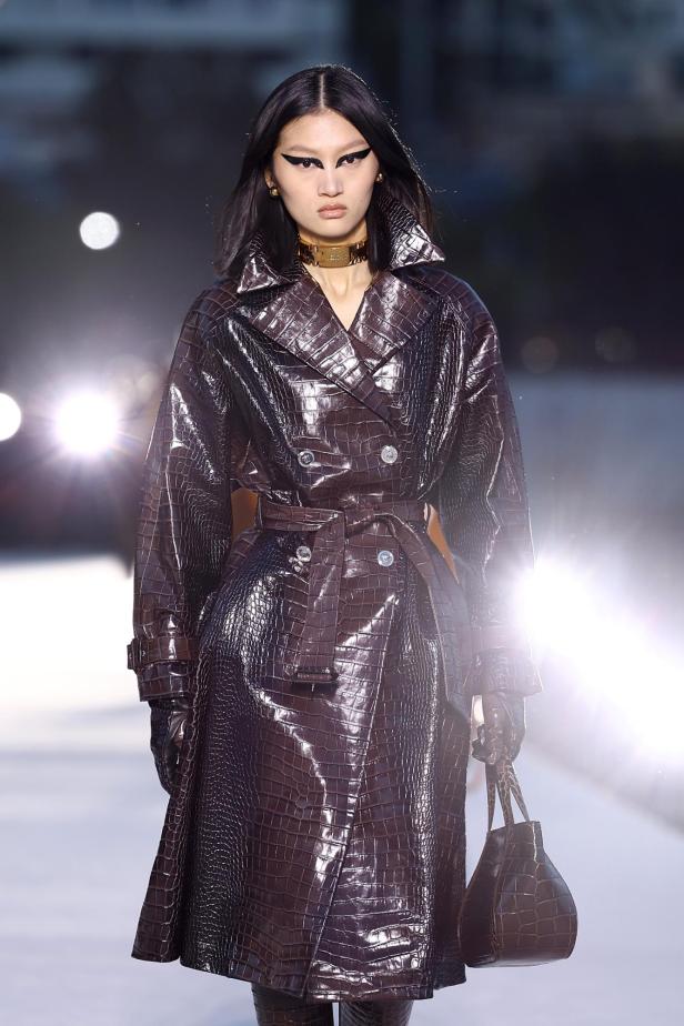 Ein Model in einem braunen Trenchcoat aus Krokodilleder bei der Versace F/W23 Show.