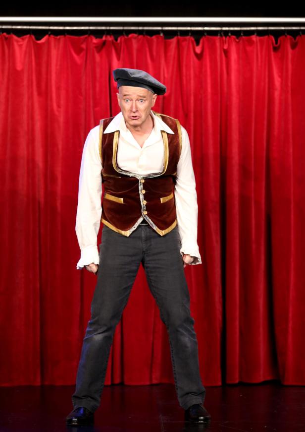 Pinnocchio, Musical Ein Mann in einem Kostüm steht vor einem roten Vorhang.
