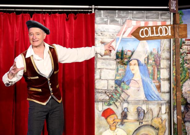 Pinnocchio, Musical Ein Mann in Kostüm steht vor einer Bühnendekoration mit Motiven aus Pinocchio.