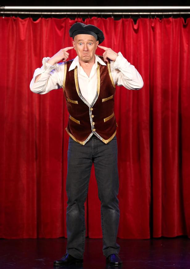 Ein Mann in einem Kostüm hält sich die Ohren zu, während er auf einer Bühne steht.