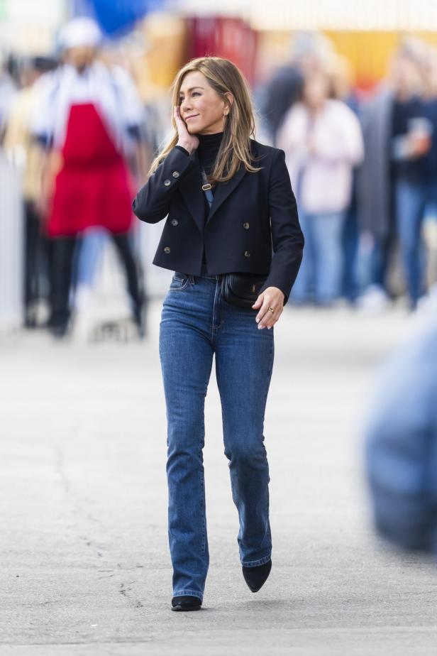 Jennifer Aniston trägt Jeans, einen schwarzen Blazer und eine Bauchtasche.