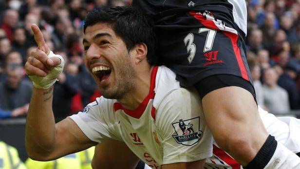 Luis Suárez jubelt mit erhobenem, bandagiertem Arm auf dem Rücken eines anderen Spielers.