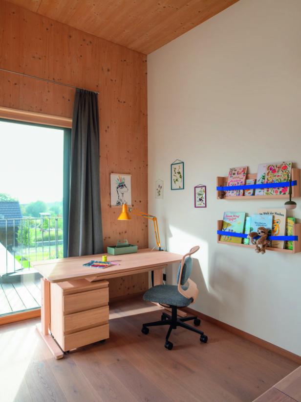 Ein Kinderzimmer mit einem Schreibtisch, einem Stuhl und Bücherregalen an der Wand.