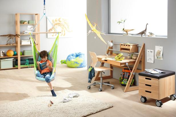 Ein Junge liest in einem Hängesessel in einem mit Dinosaurier-Dekorationen versehenen Kinderzimmer.