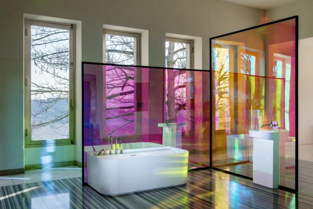 Ein Badezimmer mit einer freistehenden Badewanne und farbigen Glasscheiben, die das Licht brechen.