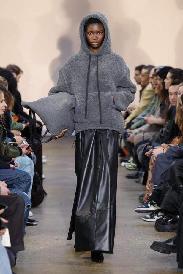Eine Frau in einem grauen Hoodie und einem langen schwarzen Rock auf einem Laufsteg.