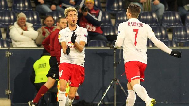 Zwei Fußballspieler in weißen und roten Trikots feiern auf dem Spielfeld.