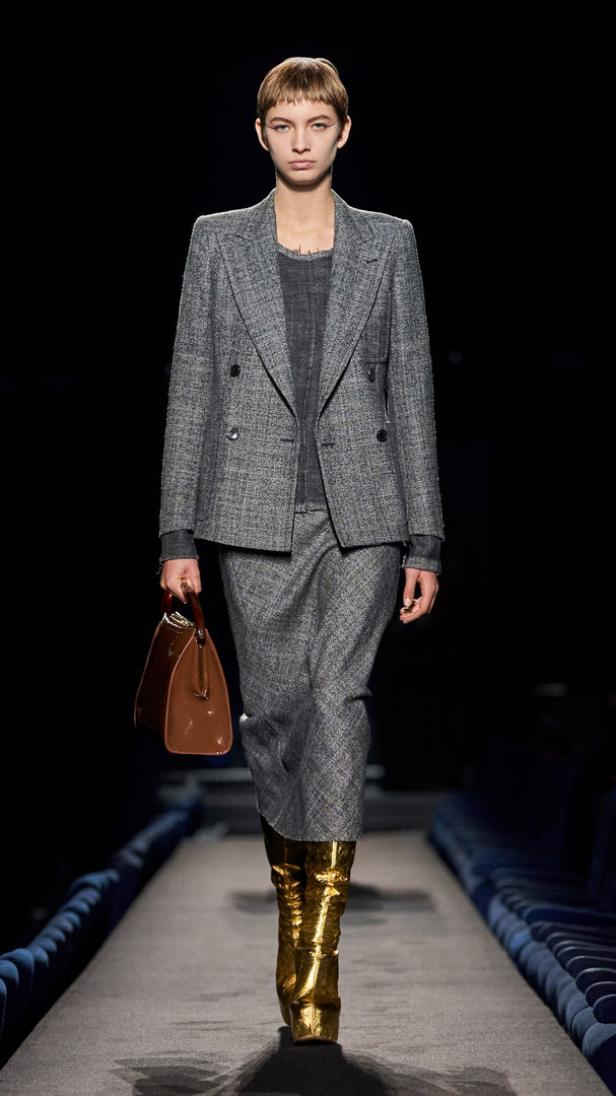 Eine Frau in einem grauen Tweed-Anzug und goldenen Stiefeln auf dem Laufsteg.