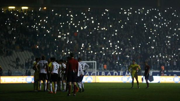 Fußballspieler stehen auf dem Spielfeld, während die Zuschauer im Stadion ihre Handys leuchten lassen.
