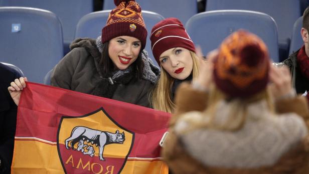 Zwei junge Frauen mit AS Rom-Mützen halten eine Vereinsflagge im Stadion.