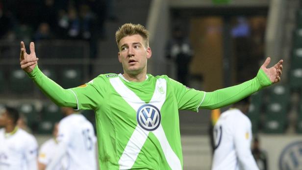 Ein Fußballspieler im grün-weißen Trikot des VfL Wolfsburg steht mit erhobenen Armen auf dem Spielfeld.