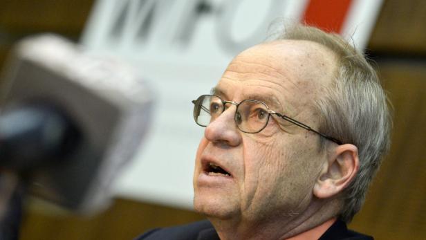 Ein älterer Mann mit Brille spricht vor einem Mikrofon.