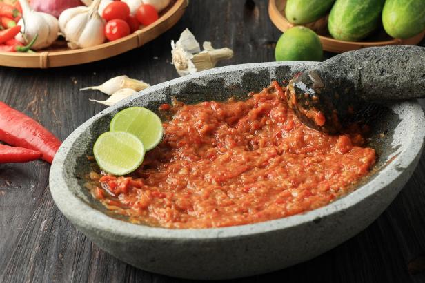 Ein Mörser mit Sambal-Soße, garniert mit Limettenscheiben, steht auf einem Holztisch.