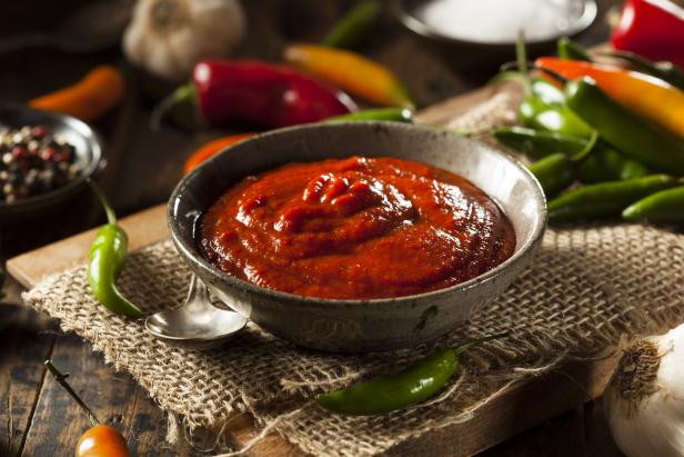 Eine Schale mit roter Chilisauce, umgeben von frischen Chilis und Knoblauch.