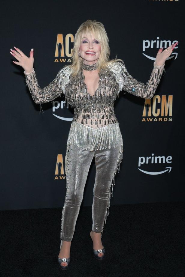 Dolly Parton posiert auf dem roten Teppich in einem silbernen Glitzeroutfit.