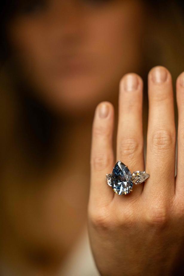 Ein tropfenförmiger blauer Diamantring an der Hand einer Frau.