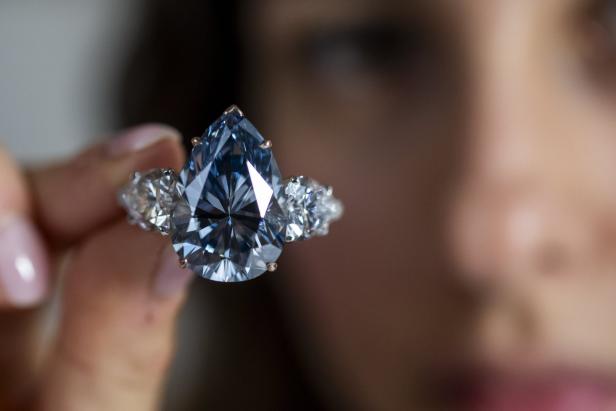 Nahaufnahme eines blauen Diamantrings in Tropfenform, der von einer Person gehalten wird.