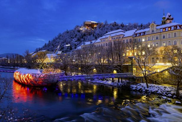 Die Murinsel und der Schlossberg in Graz sind im Winter mit Schnee bedeckt.