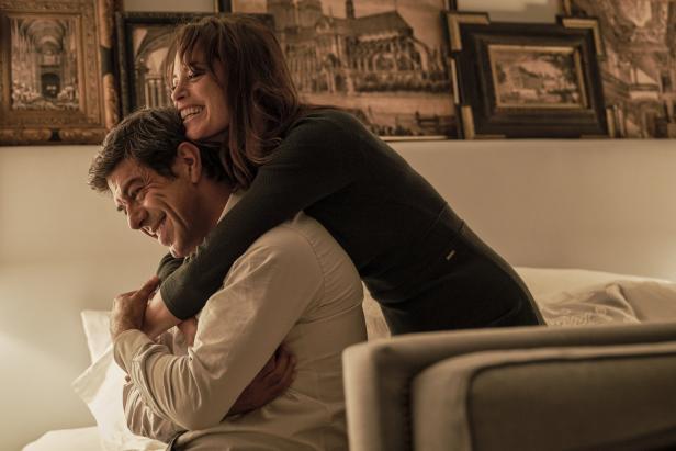 Eine Frau umarmt einen Mann von hinten, beide lächeln.