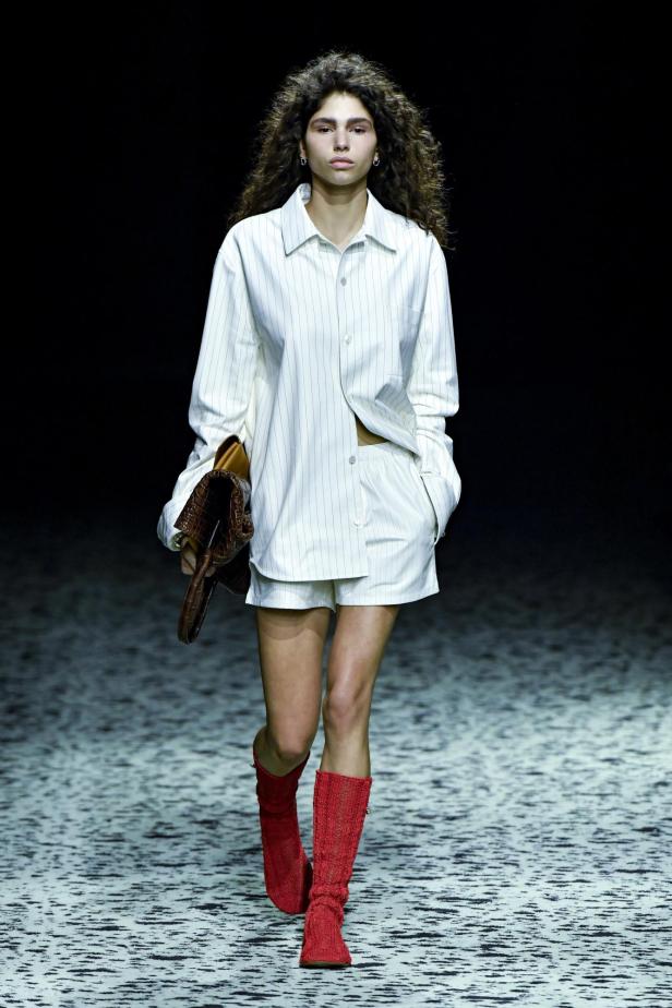 Ein Model auf dem Laufsteg in einem gestreiften Pyjama-Set und roten Stiefeln von Bottega Veneta, Herbst/Winter 2023.