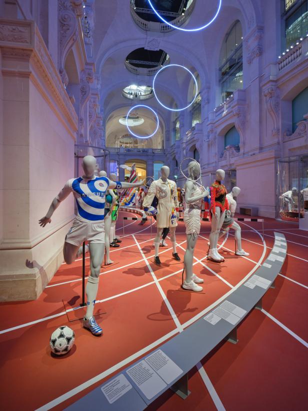 Eine Ausstellung mit Schaufensterpuppen in Sportkleidung auf einer roten Laufbahn in einem Museum.