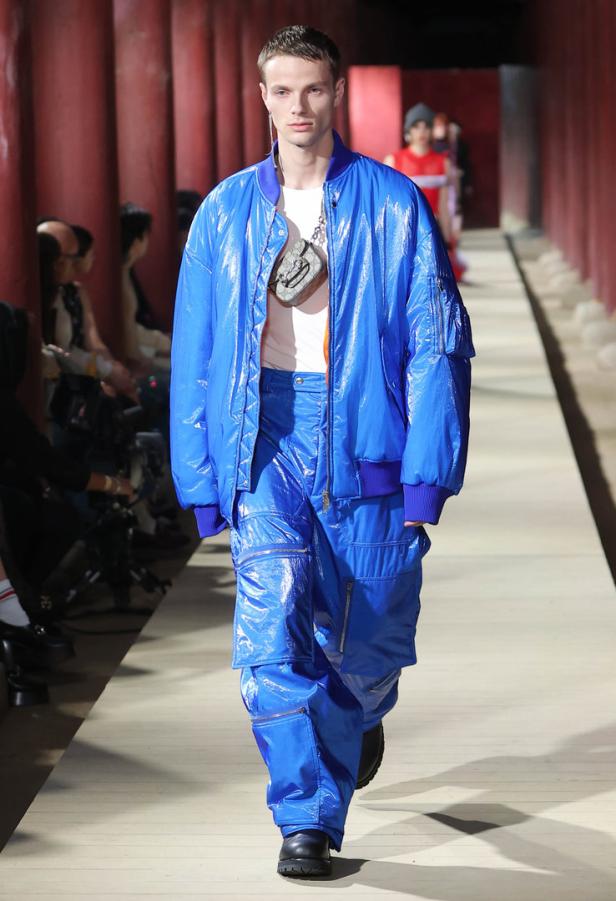 Ein Mann in einer glänzenden, blauen Jacke und Hose auf einem Laufsteg.