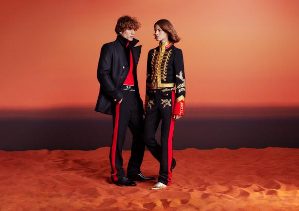 Zwei Models präsentieren elegante, von Militäruniformen inspirierte Mode auf sandigem Untergrund.